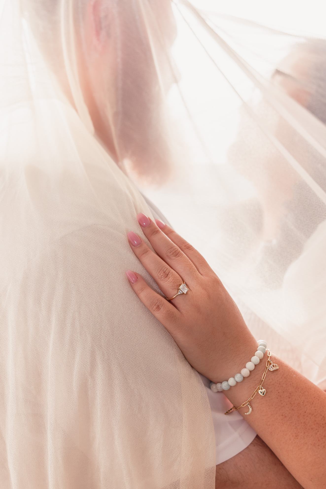 Close-up of Hope's hand and engagement ring resting on Dean under a sheer canopy, their faces softly blurred.