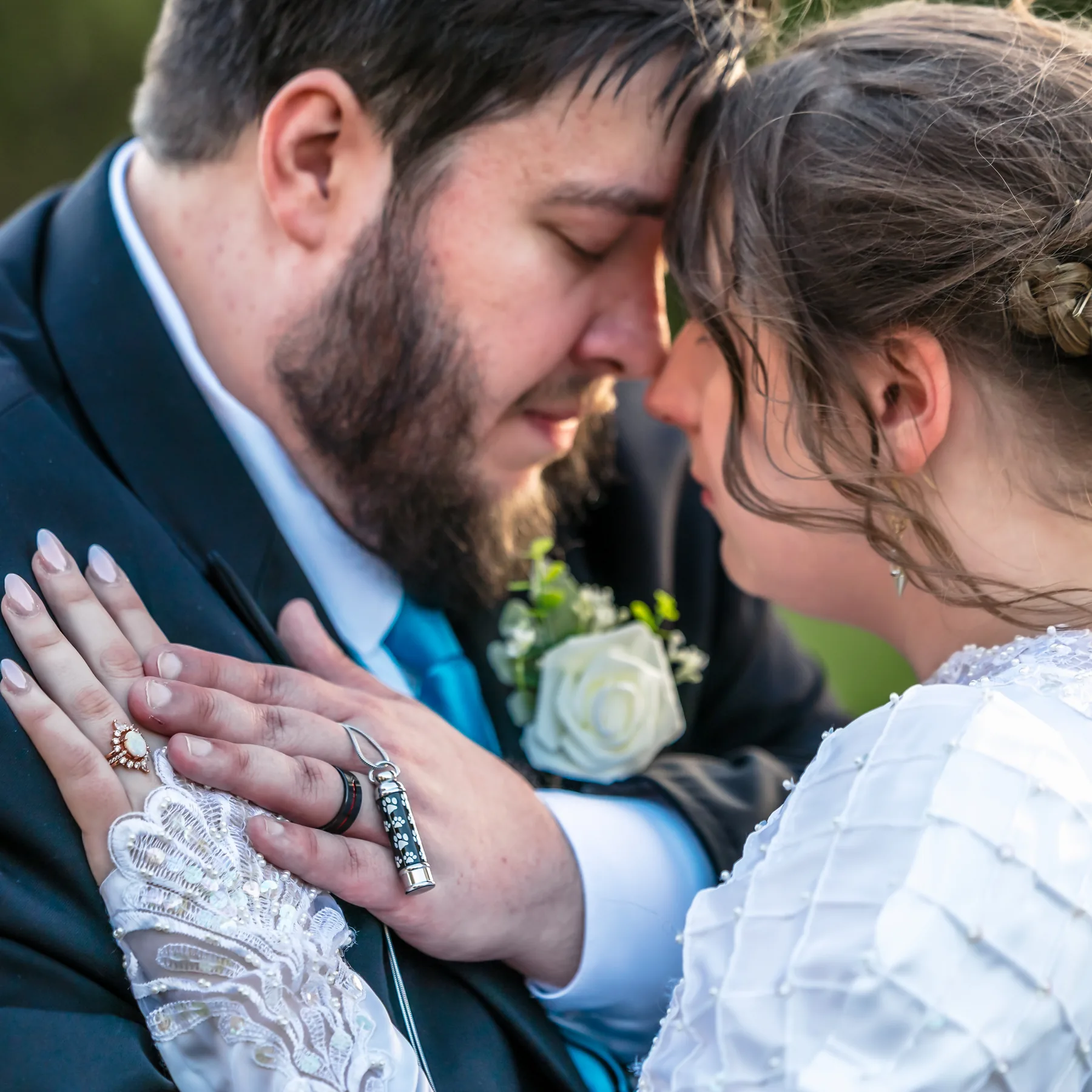 Bride and groom resting their foreheads together with eyes closed, her hand with her wedding ring on his chest